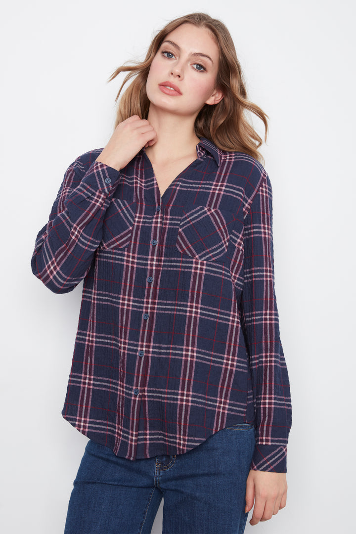 A woman wearing a navy blue long-sleeve plaid button-up shirt with red and white stripes, paired with dark blue jeans, against a plain white background.