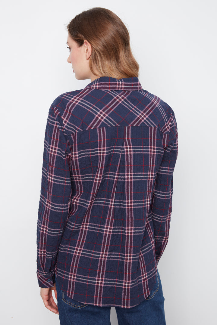 A woman shown from the back wearing a navy blue plaid button-up shirt with red and white stripes, paired with dark blue jeans, against a plain white background.