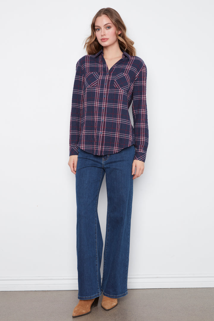 A woman shown from the back wearing a navy blue plaid button-up shirt with red and white stripes, paired with dark blue jeans, against a plain white background.