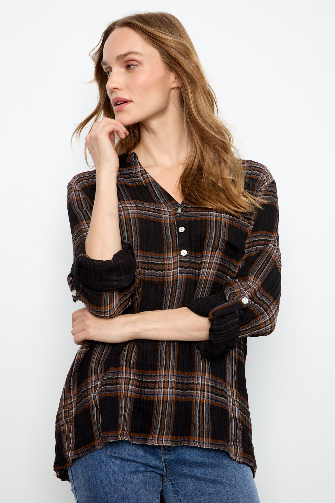 A woman wearing a black long-sleeve plaid button-up shirt with brown and beige stripes, paired with blue jeans, photographed against a plain white studio background.