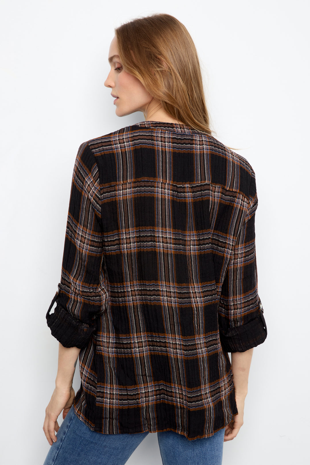 A woman shown from the back wearing a black plaid button-up shirt with brown and tan stripes, rolled up sleeves, and blue jeans against a plain white background.