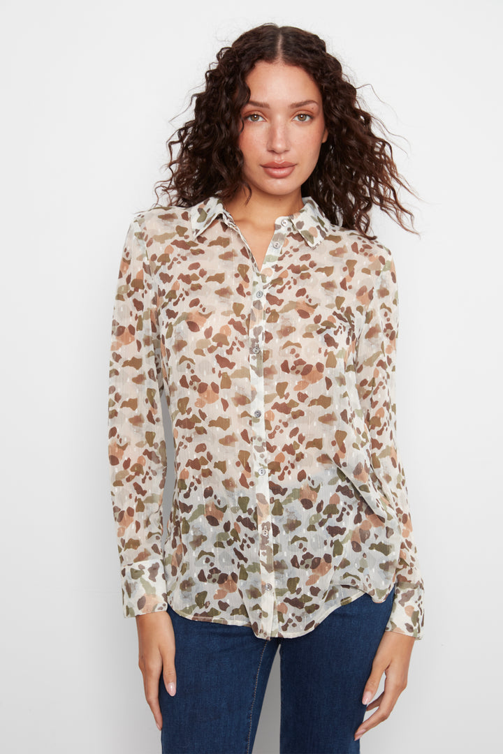 A woman wearing a long-sleeve button-up blouse with an abstract brown and tan pattern on a cream background, paired with dark blue jeans, against a plain white studio background.