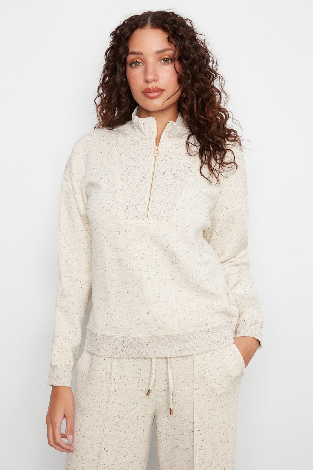 A woman modeling a cream-colored knit half-zip pullover sweater and matching drawstring sweatpants against a plain light background.