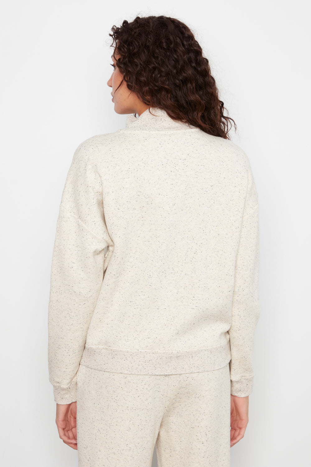 A woman shown from the back wearing a cream-colored, textured knit mock-neck top and matching knit pants against a plain white background.