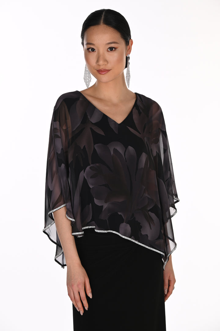 A woman modeling a sheer black V-neck blouse with a dark floral pattern and layered flutter sleeves, paired with a black skirt against a plain white studio background.