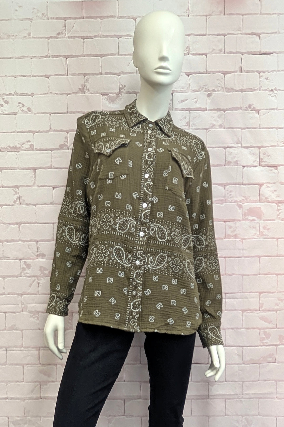 A long-sleeve button-up shirt with a brown and white paisley bandana print, displayed on a white mannequin against a light pink brick wall.