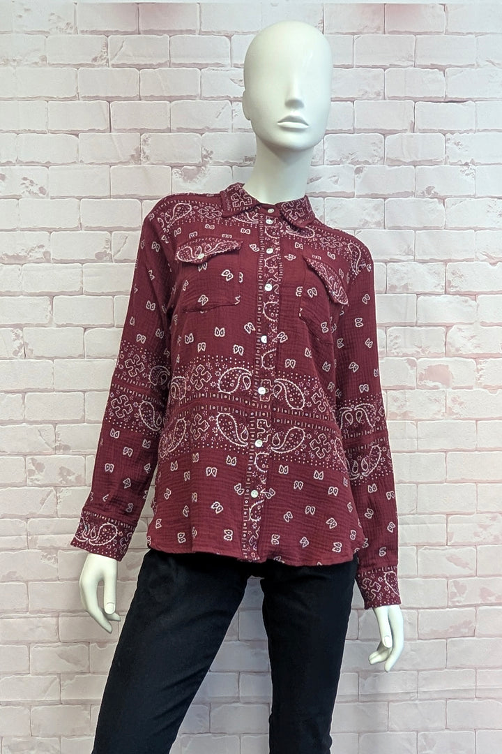 A long-sleeve button-up shirt in a deep burgundy red with a white paisley and floral bandana print, displayed on a white mannequin against a light brick wall.