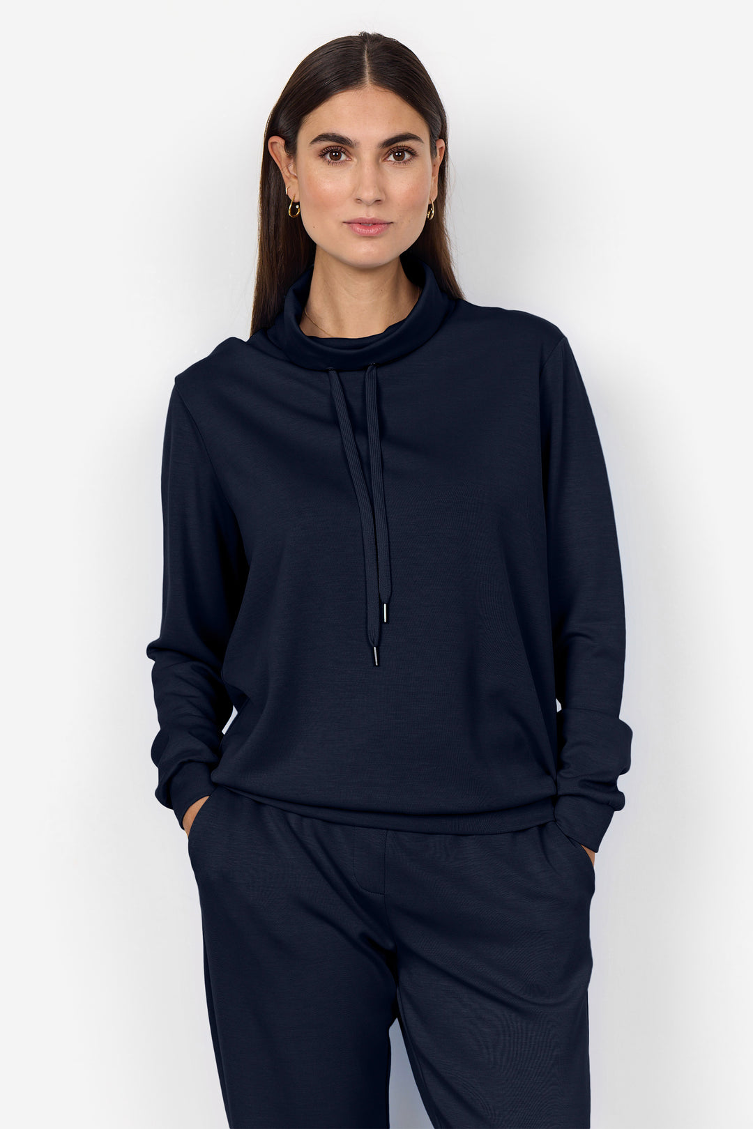 A woman modeling a dark navy blue sweatshirt and matching sweatpants set against a plain light gray background.