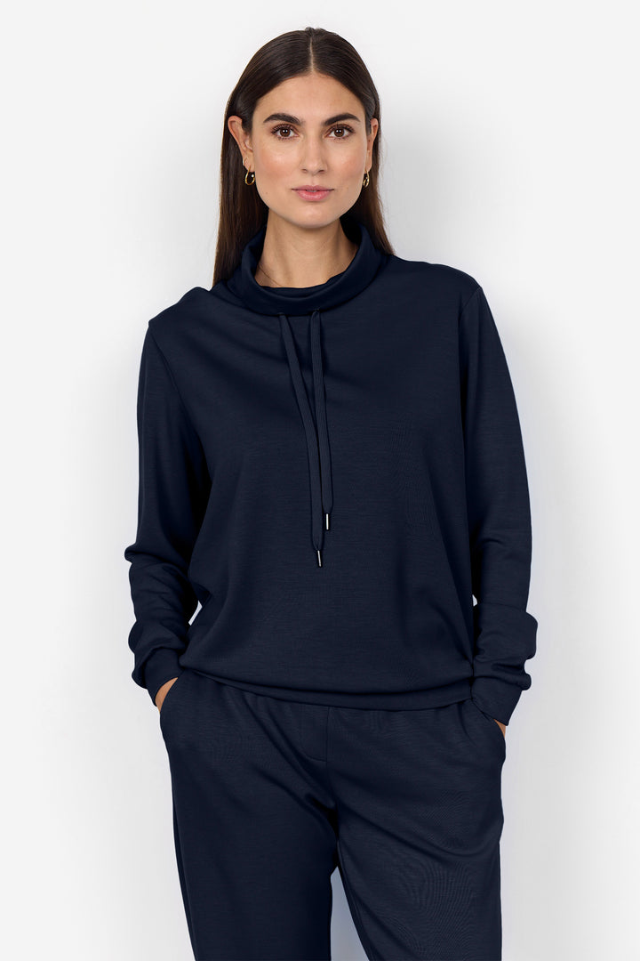 A woman modeling a dark navy blue sweatshirt and matching sweatpants set against a plain light gray background.