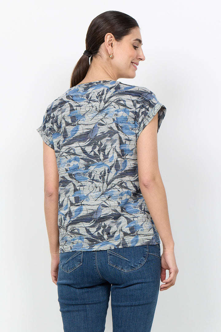 A woman shown from the back wearing a short-sleeve top with a blue, gray, and white abstract pattern, paired with dark blue jeans, against a plain white background.