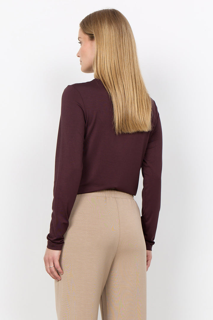 A woman with long blonde hair is shown from the back wearing a dark plum long-sleeve crop top and beige pants against a plain white background.