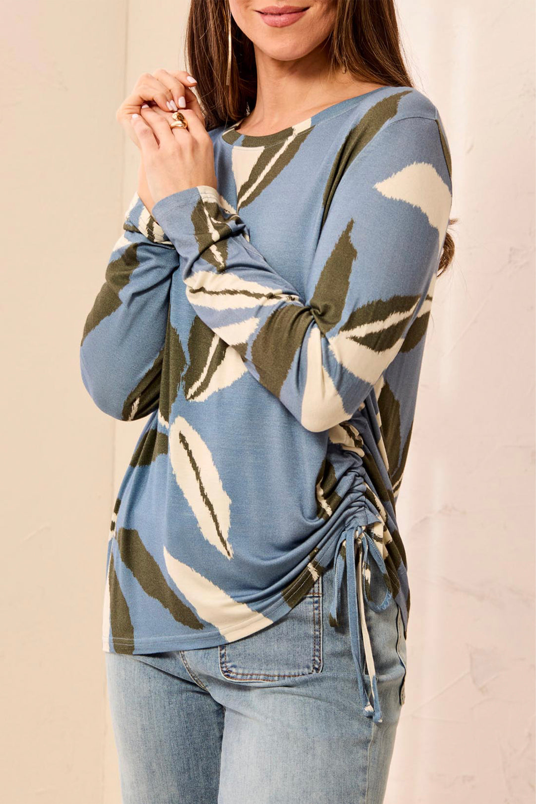 Woman wearing a blue long-sleeve top with leaf pattern and tied front, standing against a beige background.