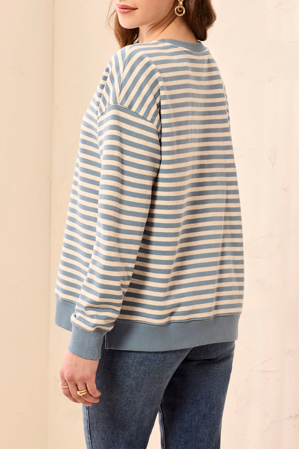 A woman wearing a light blue and cream striped long-sleeve sweatshirt with solid light blue ribbed cuffs and hem, paired with blue jeans.