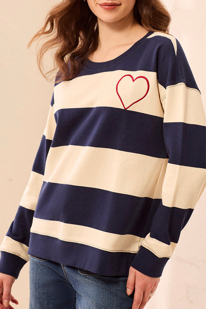 Person wearing a navy and white striped sweater with a red heart design on a beige background