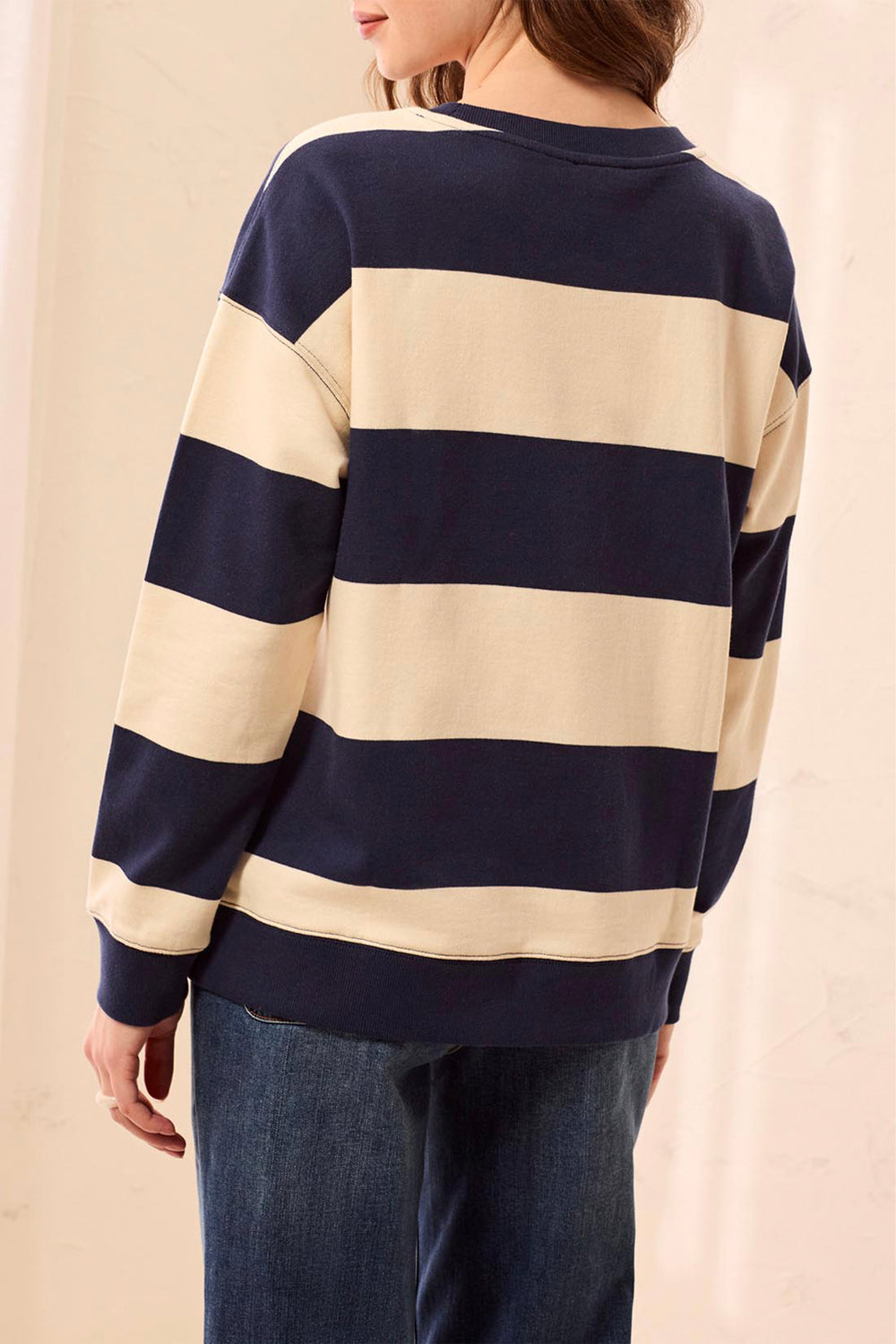 A person shown from the back wearing a navy and cream striped long-sleeve sweater with blue jeans, set against a soft beige background.