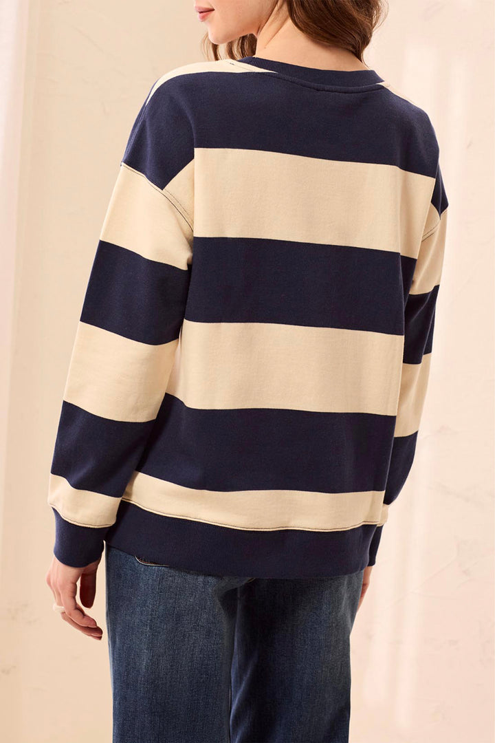 A person shown from the back wearing a navy and cream striped long-sleeve sweater with blue jeans, set against a soft beige background.