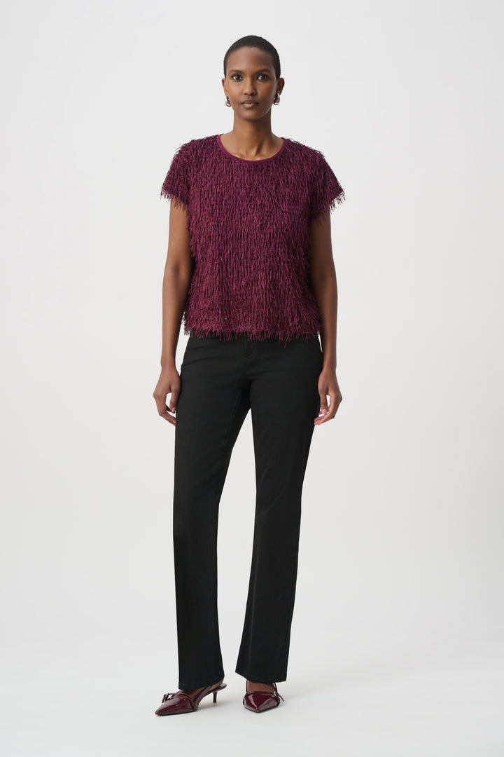 Woman wearing a maroon textured top and black pants on a white background