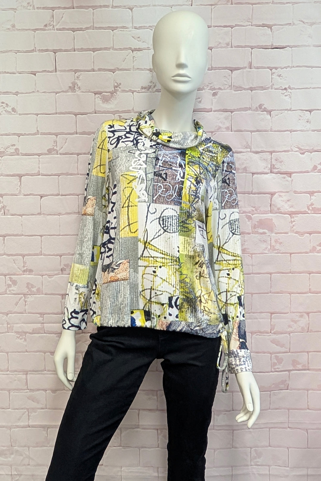 A long-sleeve abstract print blouse displayed on a white mannequin, paired with black pants, set against a light pink brick wall background.