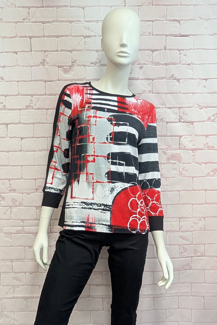 A long-sleeve abstract knit top in red, black, and white, displayed on a female mannequin against a light pink brick wall background.
