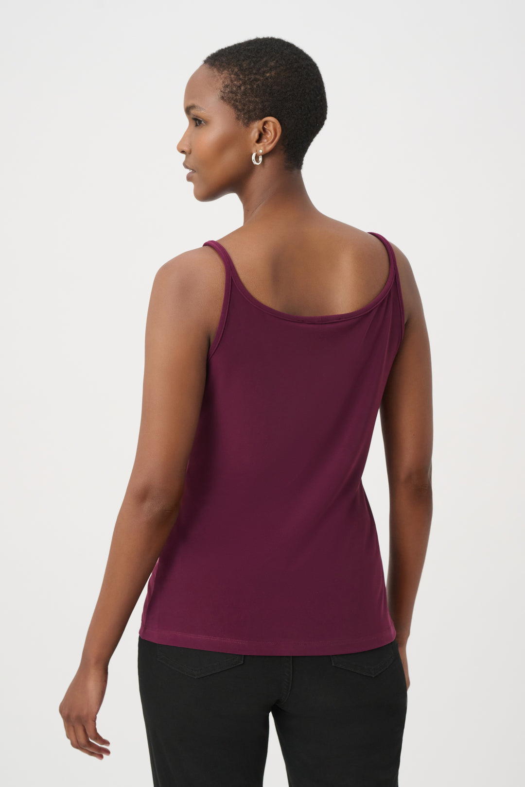 A woman shown from the back wearing a sleeveless scoop-neck tank top in deep burgundy and black pants, photographed against a plain light gray studio background.