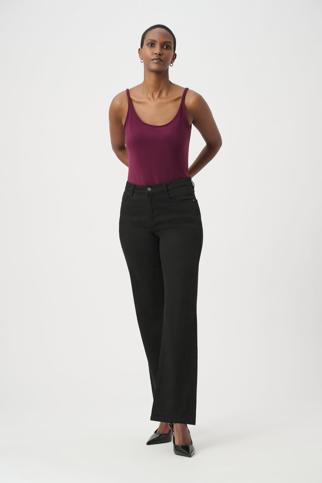 A woman modelling a purple coloured basic thin strapped camisole wearing black pants and shoes in front of a white background. 