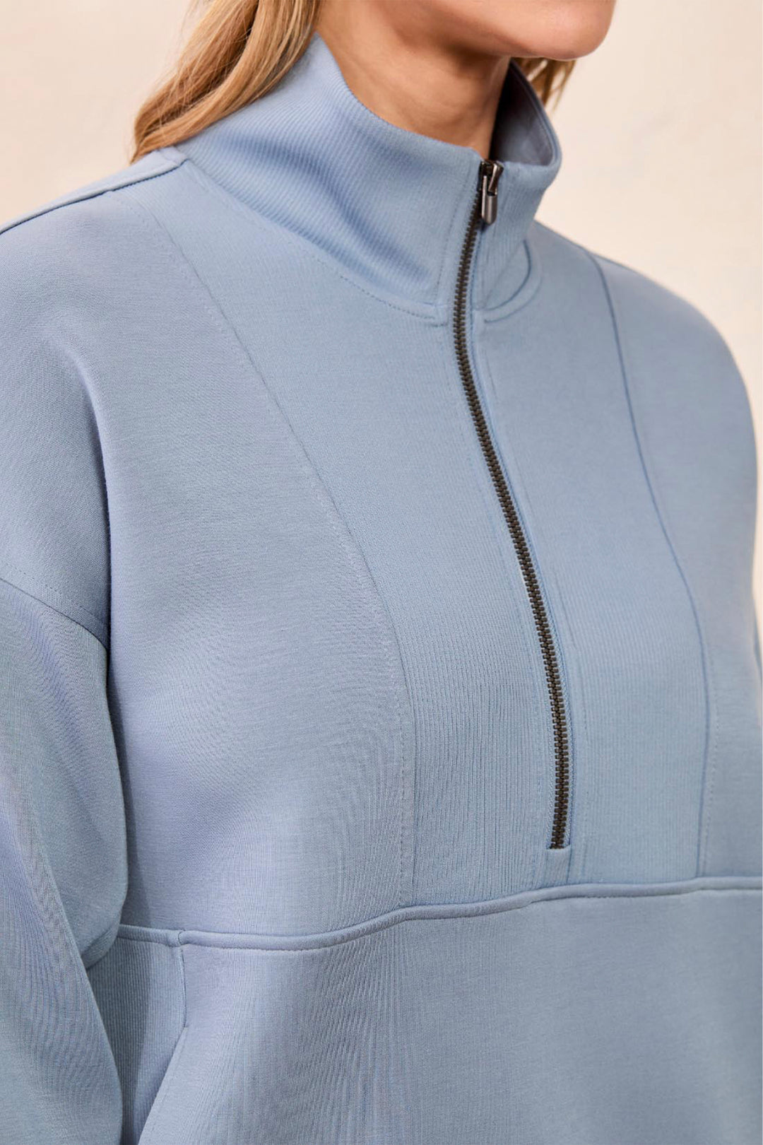 A close-up of a person wearing a light blue ribbed half-zip pullover with a mock neck collar and a black zipper.