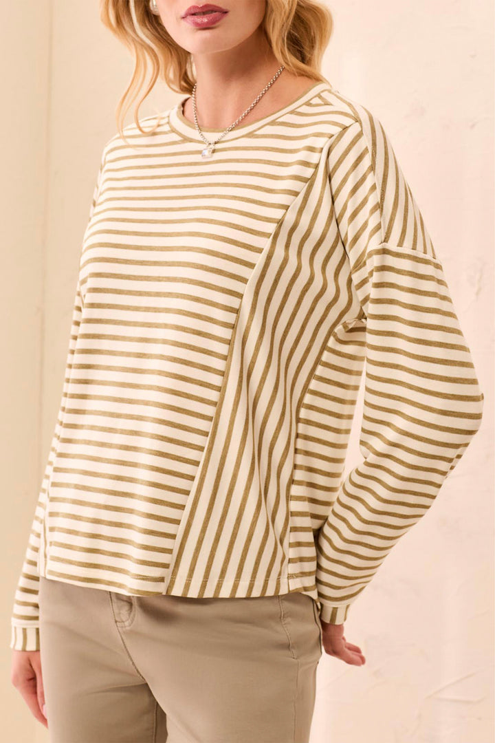 A woman wearing a cream and olive green striped long-sleeve top with a crew neck, paired with khaki pants, against a light beige background.