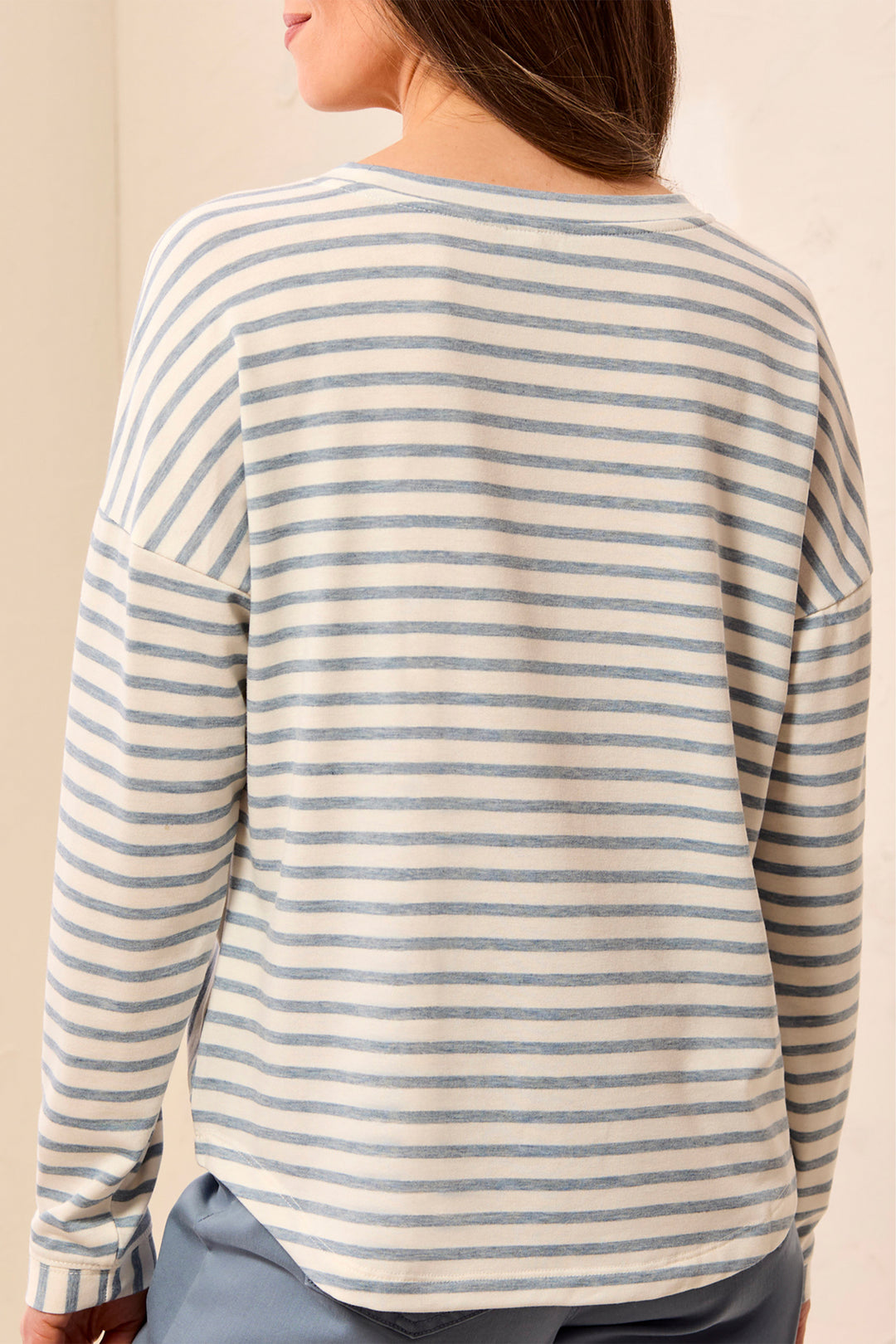 A woman shown from the back wearing a long-sleeve striped top with horizontal light blue and cream stripes, paired with gray pants.
