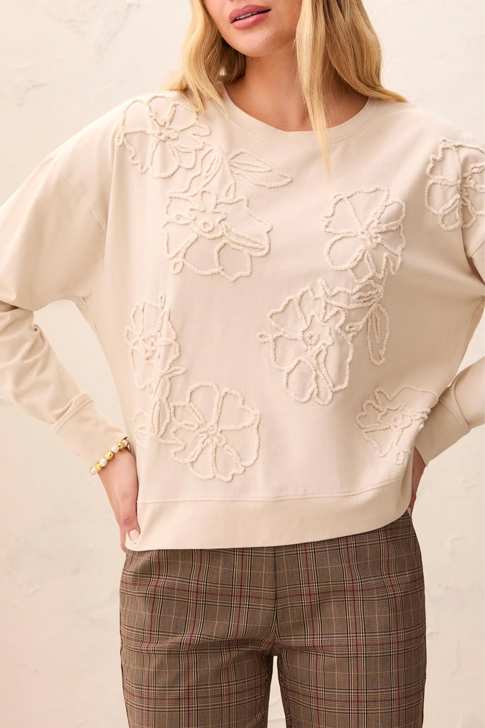 Beige sweater with floral embroidery worn by a person, against a neutral background