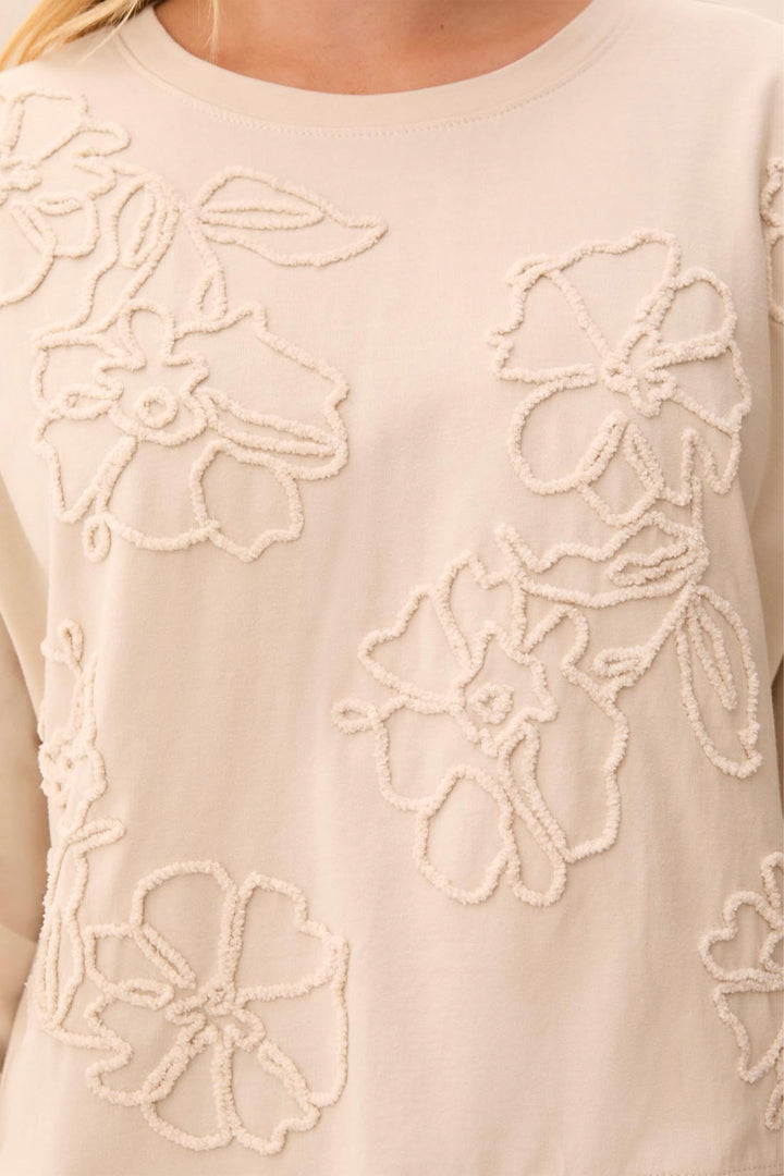 Close-up of a cream-colored long-sleeve top with textured floral embroidery on the front, worn by a model.