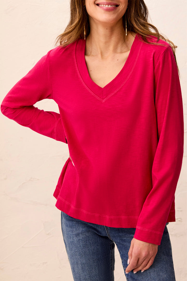 A woman wearing a bright pink long-sleeve V-neck top and blue jeans, shown from the nose down against a light beige wall.