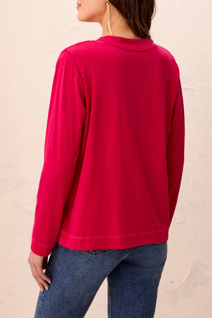 A woman shown from the back wearing a bright pink long-sleeve top and blue jeans, standing against a textured beige wall.