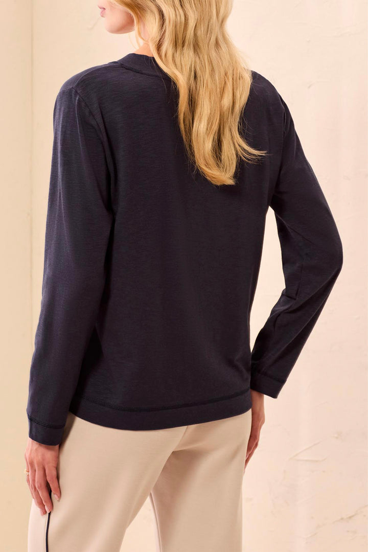 A woman shown from the back wearing a dark navy long-sleeve top and blue jeans, standing against a textured beige wall.