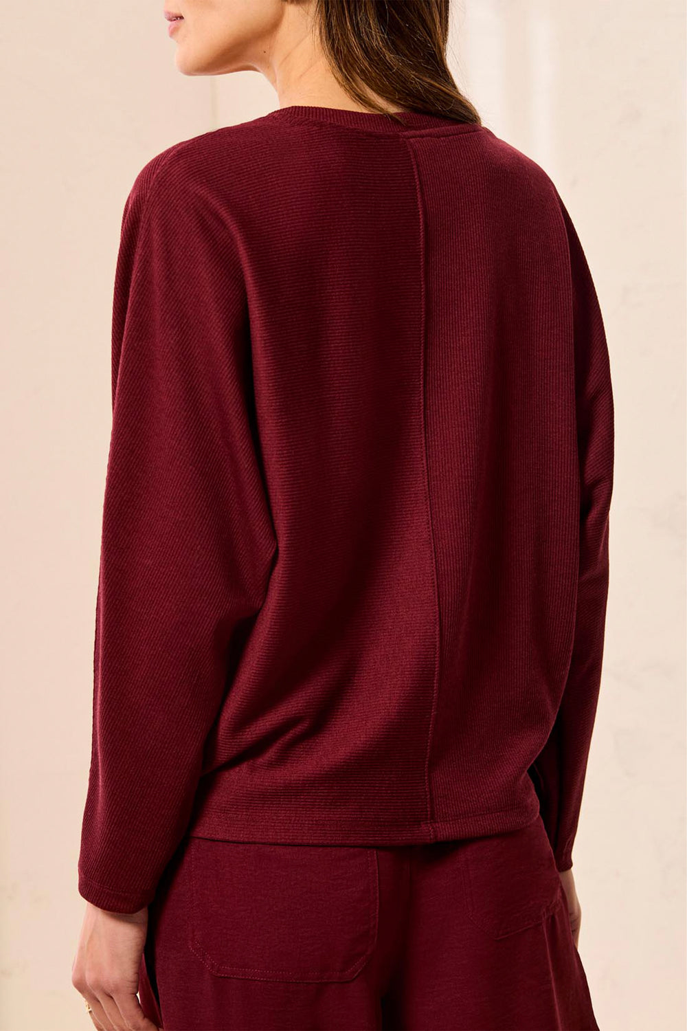 A woman shown from the back wearing a long-sleeve knit top and matching bottoms in a deep burgundy color, against a warm off-white background.