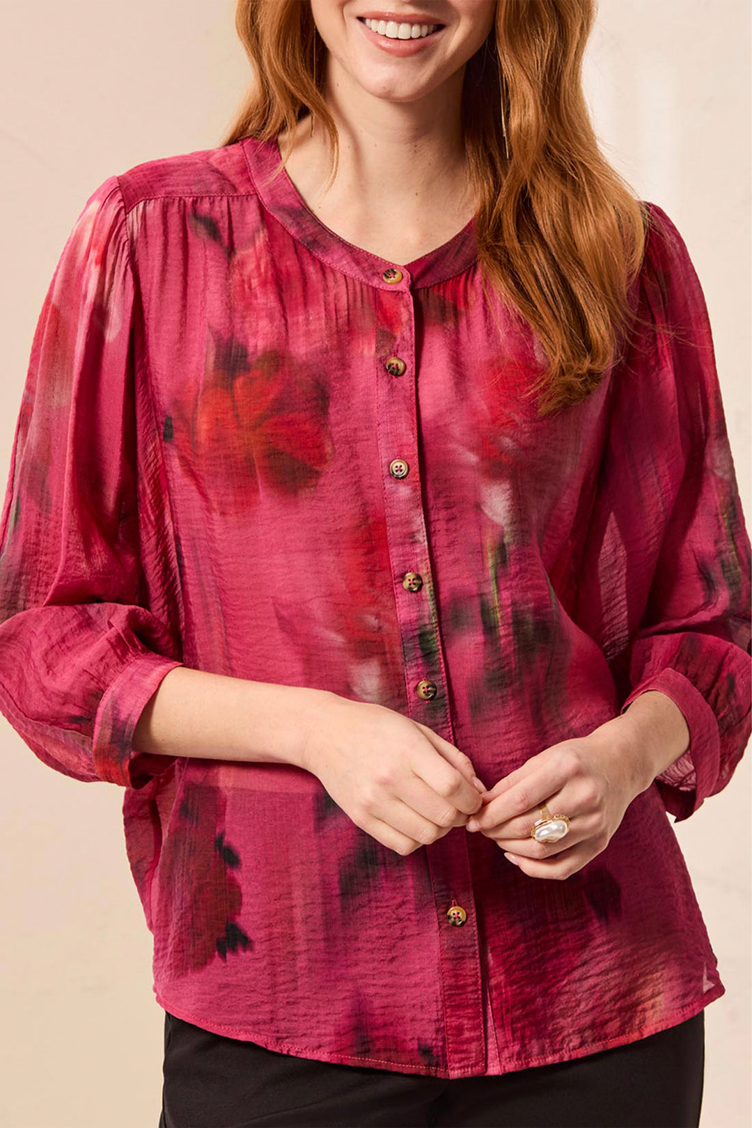 A woman wearing a long-sleeve button-front blouse in a deep magenta pink with a dark floral print, shown against a plain beige background.