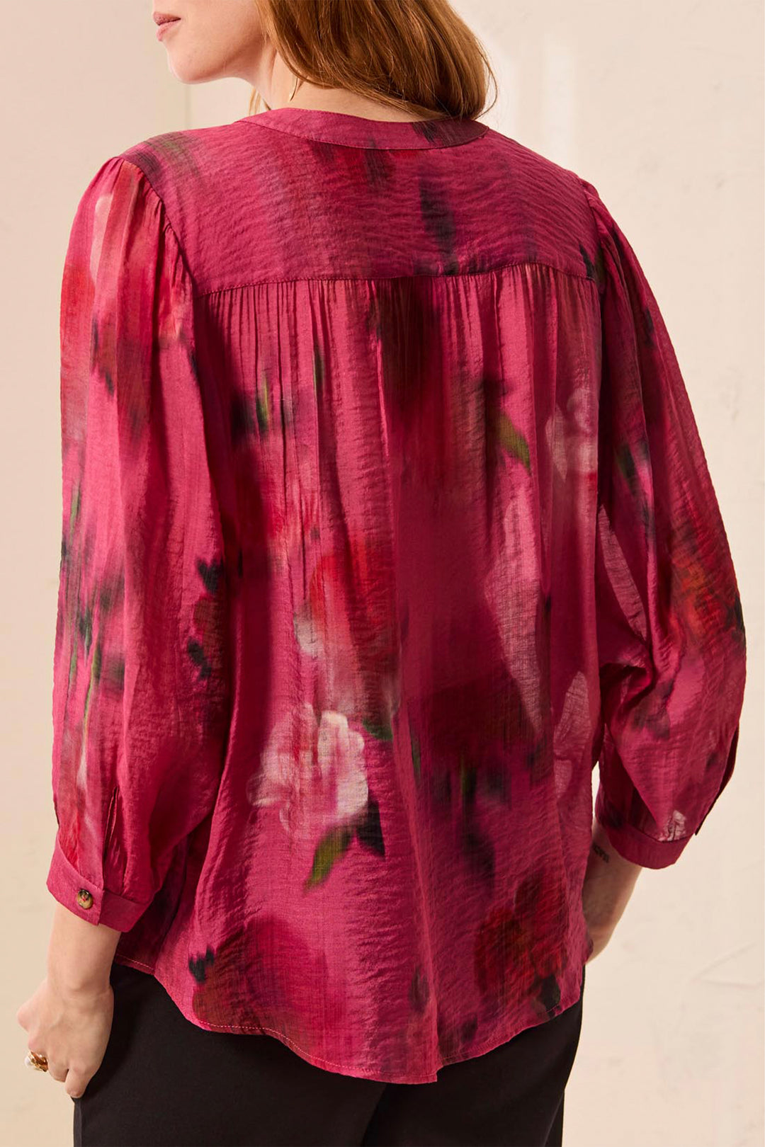 A woman shown from the back wearing a long-sleeve, crinkled chiffon blouse with a dark red and magenta floral print, paired with black pants.