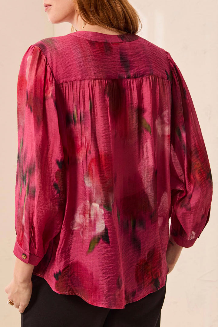 A woman shown from the back wearing a long-sleeve, crinkled chiffon blouse with a dark red and magenta floral print, paired with black pants.