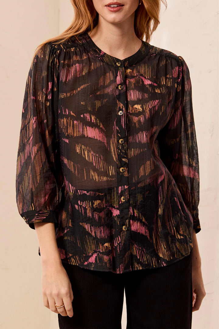 A woman modelling a black leaf print loose blouse in front of a light beige background. 
