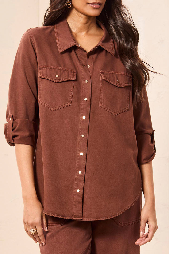 A woman wearing a rust-brown button-up shirt with three-quarter sleeves and matching brown pants, shown against a plain light background.