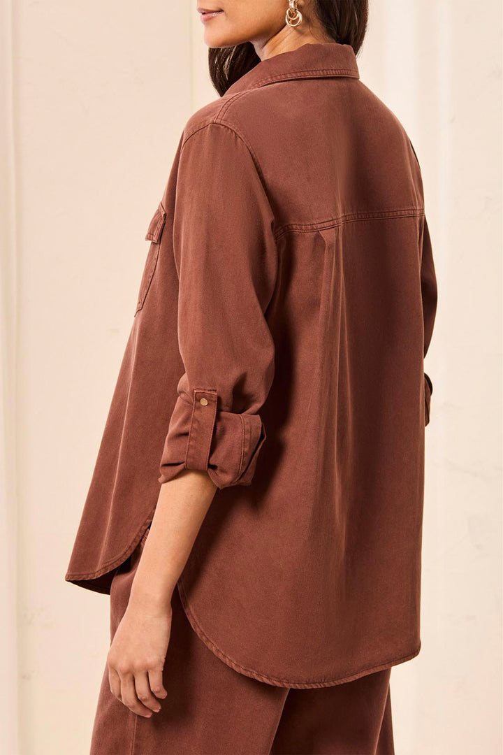 A woman shown from the back wearing a rust-brown button-up shirt with three-quarter sleeves and matching brown pants, shown against a plain light background.