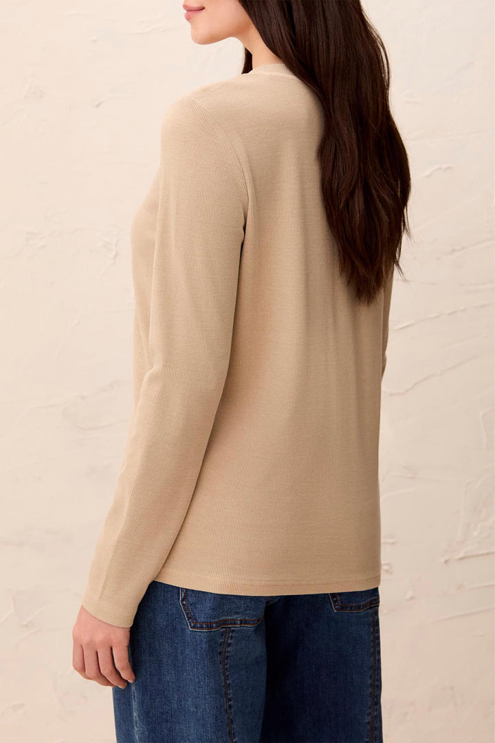 A woman shown from the back wearing a beige long-sleeve knit top and blue jeans against a light textured wall.