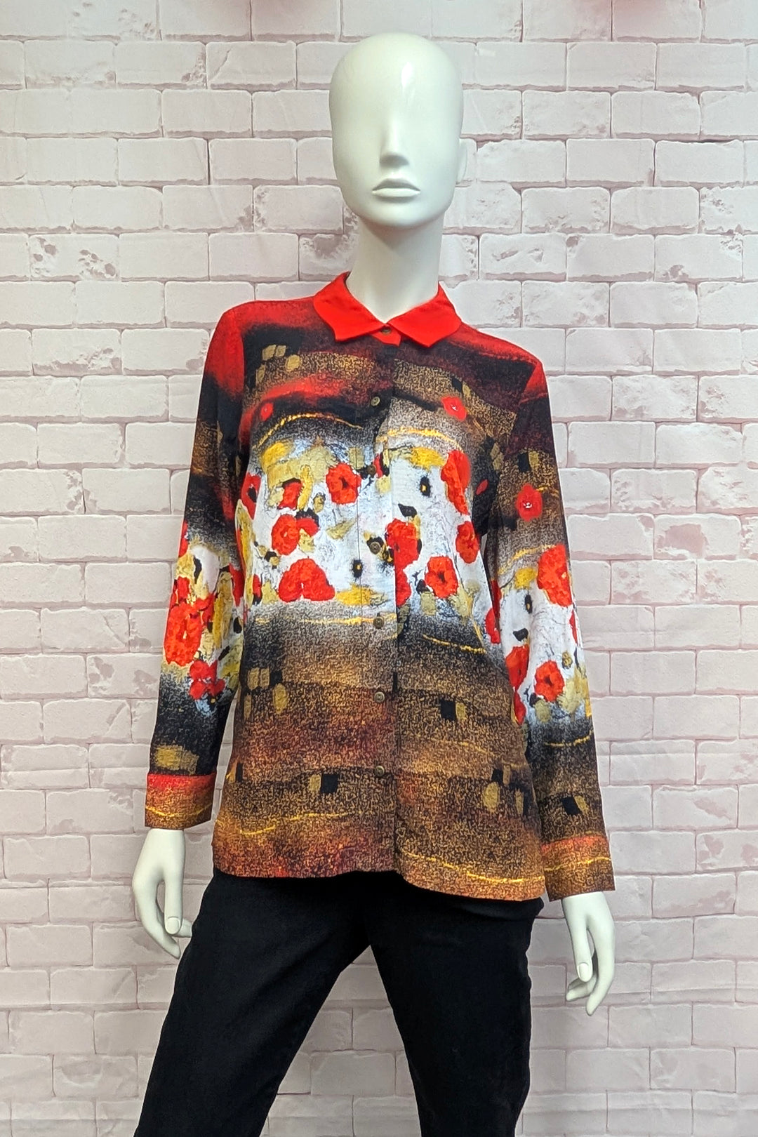 A women's mannequin wearing a long-sleeve collared shirt with a vibrant red collar and cuffs, featuring an artistic print of red poppies over a brown and white landscape. 