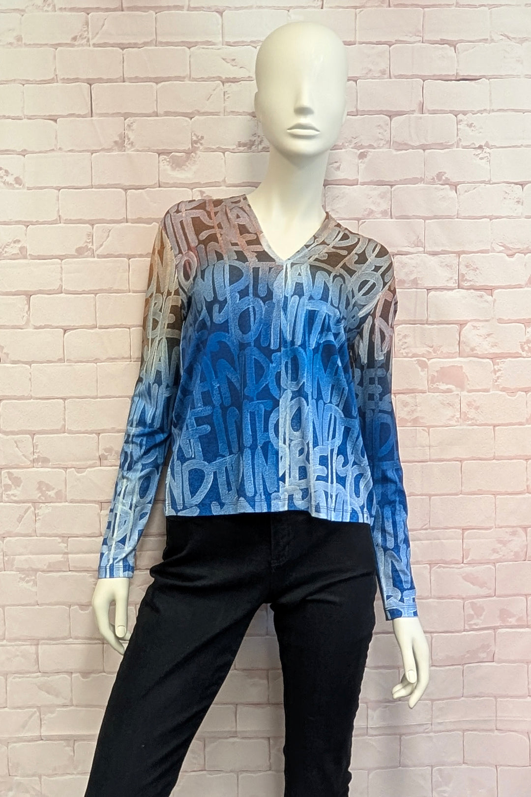 A mannequin modelling a women's long-sleeve V-neck top featuring a colorful abstract graffiti-style print with a gradient transition from peach and orange at the shoulders to light blue, medium blue, and white at the hem.