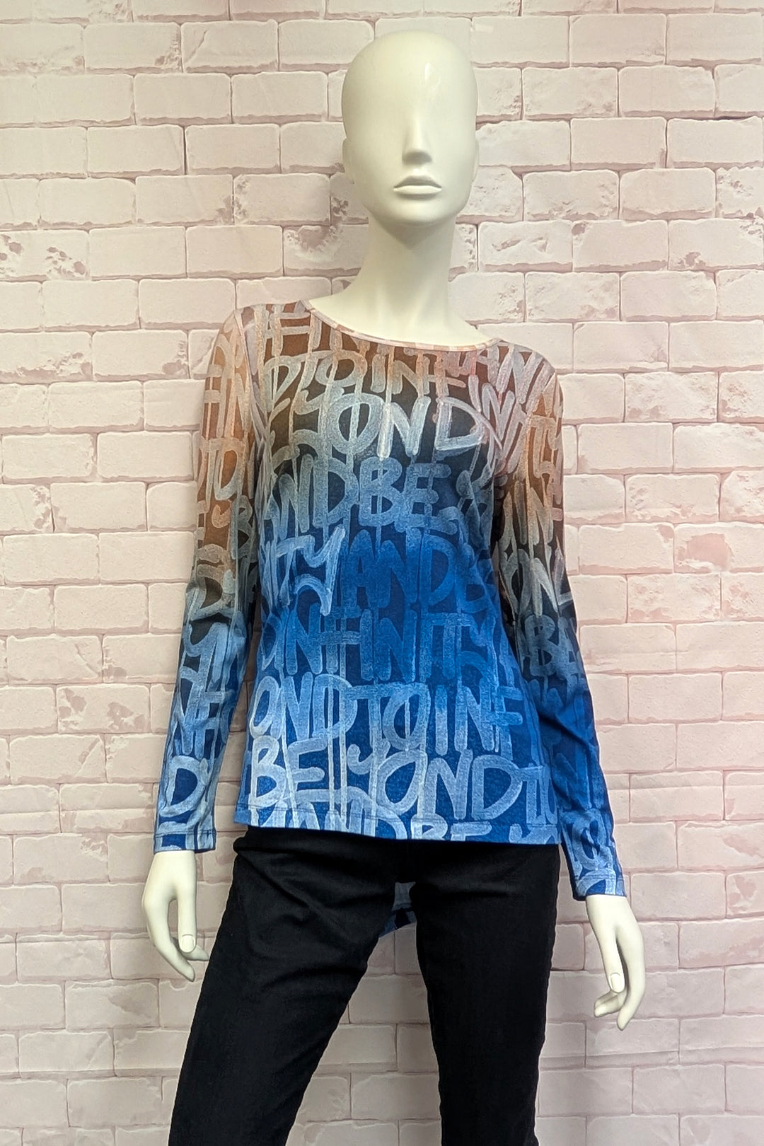 A mannequin wearing a women's long-sleeve top with a high-low hem, featuring a gradient color transition from peach-orange at the shoulders to light blue and medium blue at the hem. 