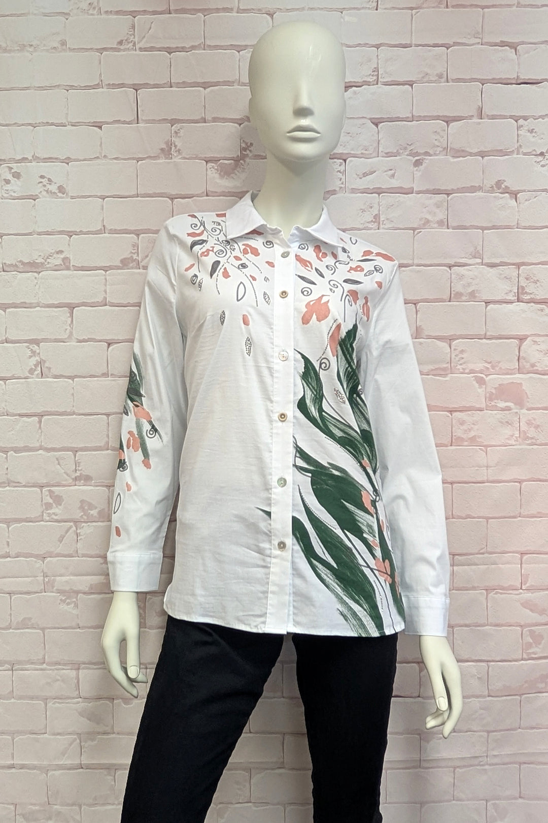 A mannequin wearing a white long-sleeve button-up shirt with a printed botanical pattern featuring green leaves, peach flowers, and gray swirls.