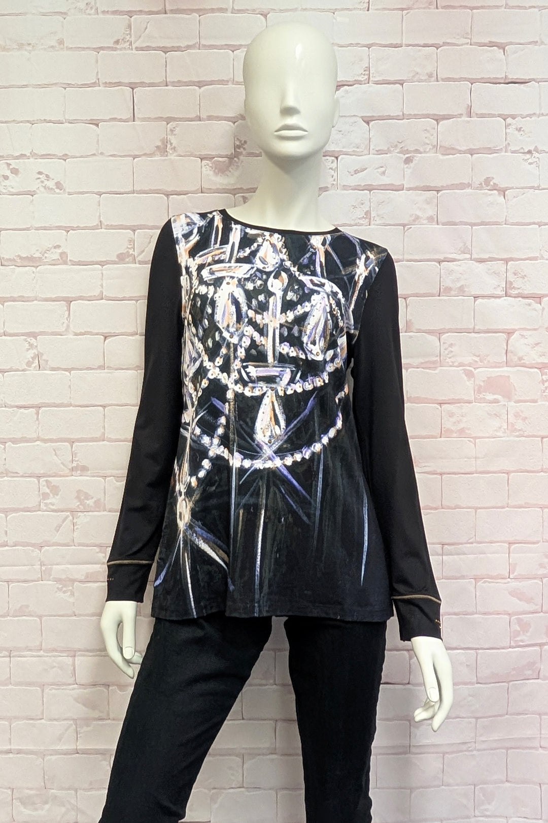 A mannequin wearing a long-sleeve tunic top in dark brown with a large graphic print of chandeliers and pearls in silver, white, and light purple tones across the front.