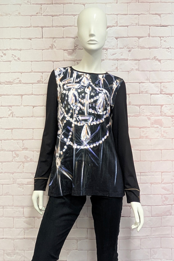A mannequin wearing a long-sleeve tunic top in dark brown with a large graphic print of chandeliers and pearls in silver, white, and light purple tones across the front.