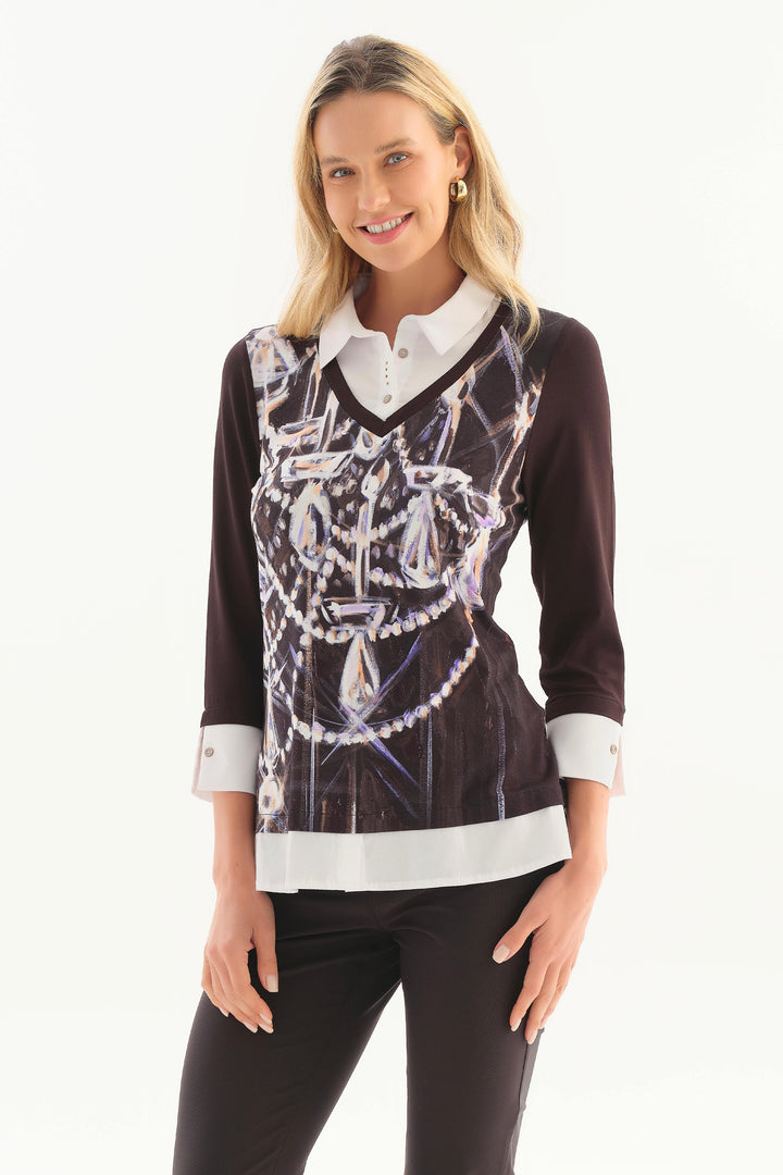 A woman modeling a long-sleeve collared top with a black base, white collar and hem, and a large front graphic print featuring white and silver chains and gem-like details, paired with black pants against a white studio background.