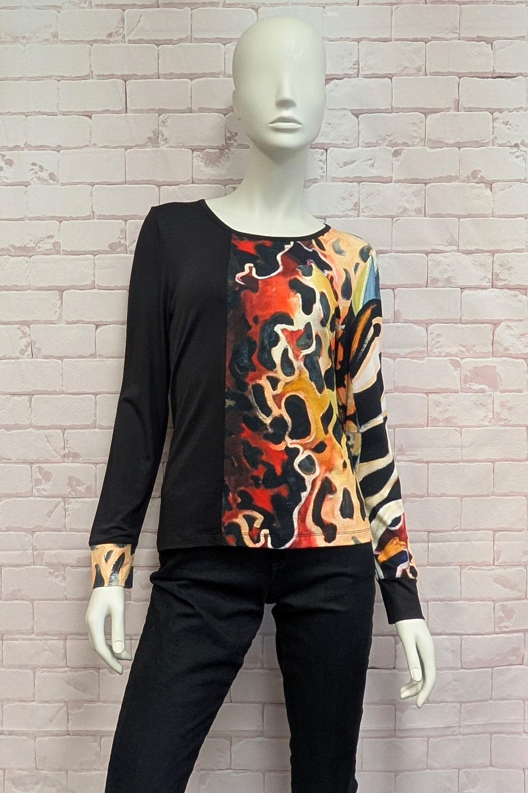 A mannequin wearing a women's long-sleeve top with a color-blocked design, featuring a solid dark brown left side and sleeve, and a right side with a bold abstract print in orange, black, white, and yellow.