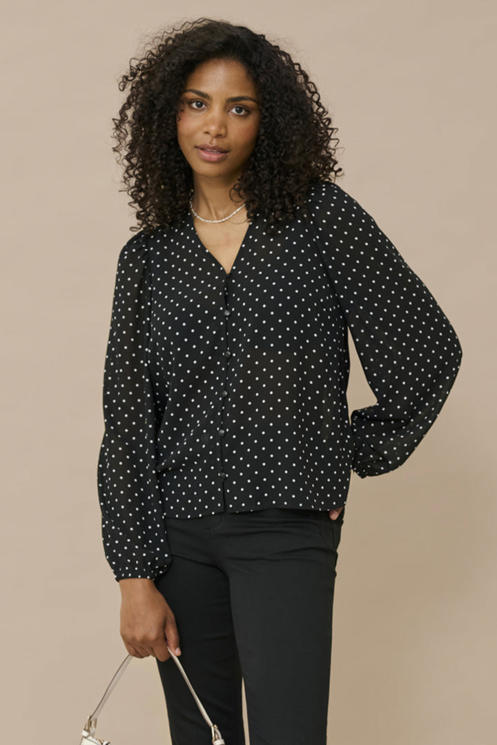 A woman wearing a black polka dot blouse and black pants. 